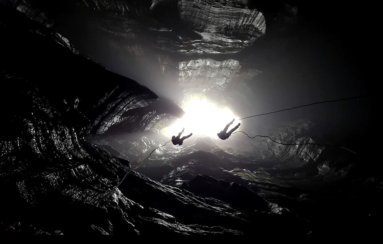 Two climbers abseiling into a cave