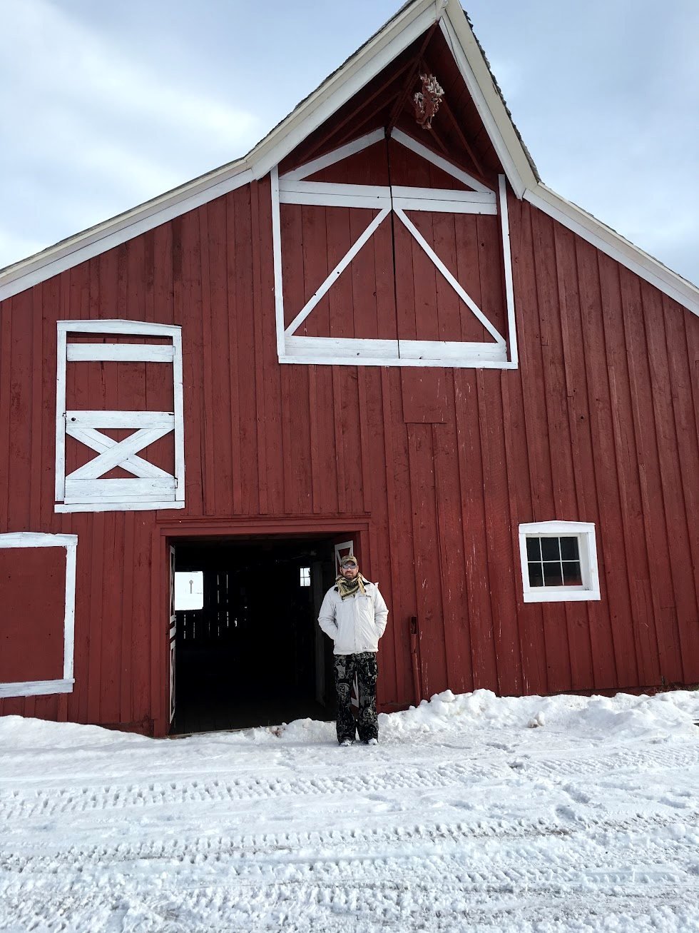 Mark in the snow outside a red barn
